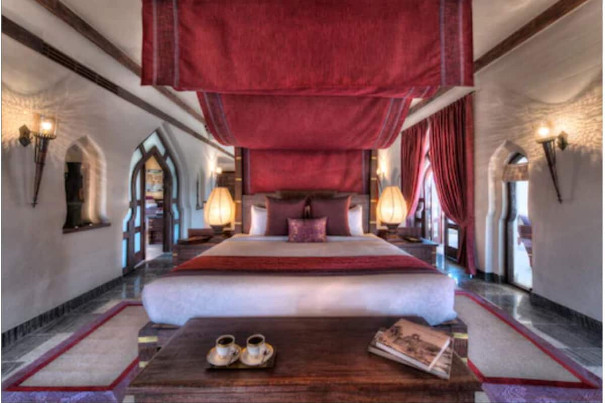 A large bed with a red canopy, two bedside tables with lamps, and a wooden side table with a book and slippers.
