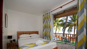 A hotel room with a bed, a nightstand, a chair, and a view of palm trees and the beach. - Bluewaves Beach House (Boracay Island)