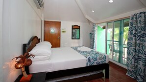 A bedroom with a bed, a wooden headboard, a wall-mounted air conditioner, a door, a window with a view, and a curtain with a leaf pattern. - Bluewaves Beach House (Boracay Island)