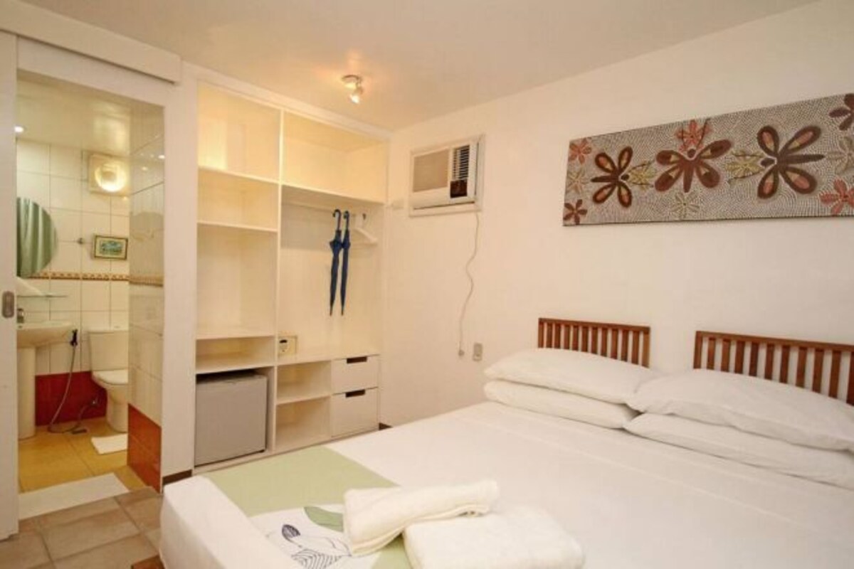 A bedroom with a bed, a wardrobe, a mirror, and a wall-mounted air conditioner.