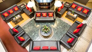 A modern lounge area with multiple black sofas and armchairs, each with red cushions. A central coffee table with a floral arrangement is surrounded by a patterned floor. - HM Suites & Studios Bangalore (Bengaluru)