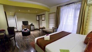 A hotel room with a large bed, a desk, a chair, a small kitchenette, and a TV. - HM Suites & Studios Bangalore (Bengaluru)