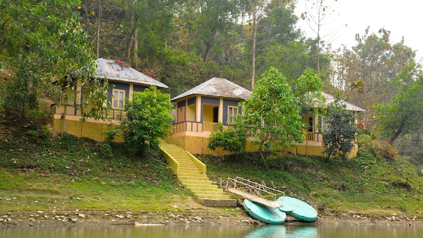Un chalet au bord du lac, avec un escalier menant à l’entrée, entouré d’une végétation luxuriante.