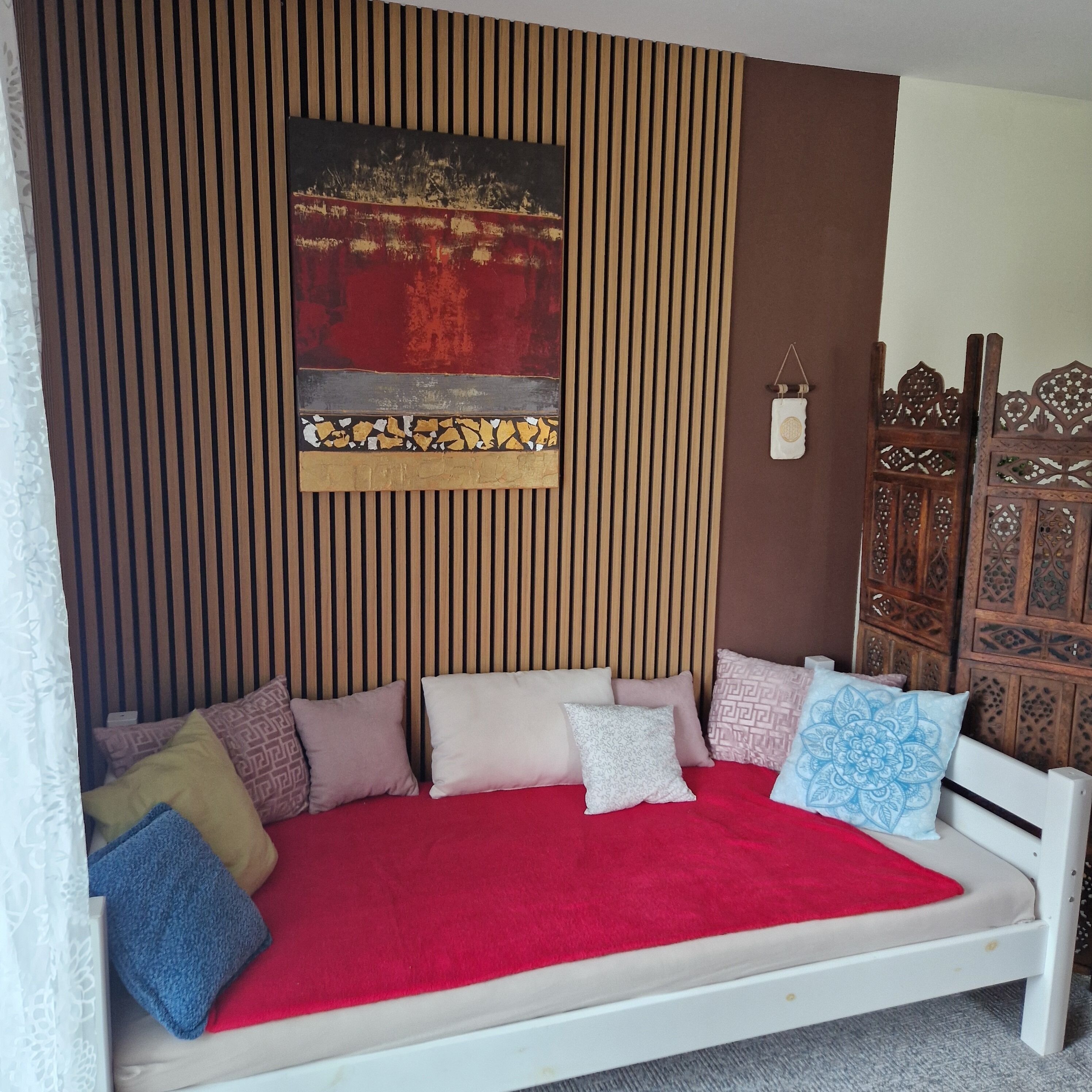 A room with a white sofa bed, a red throw blanket, and a wall with vertical wooden slats.