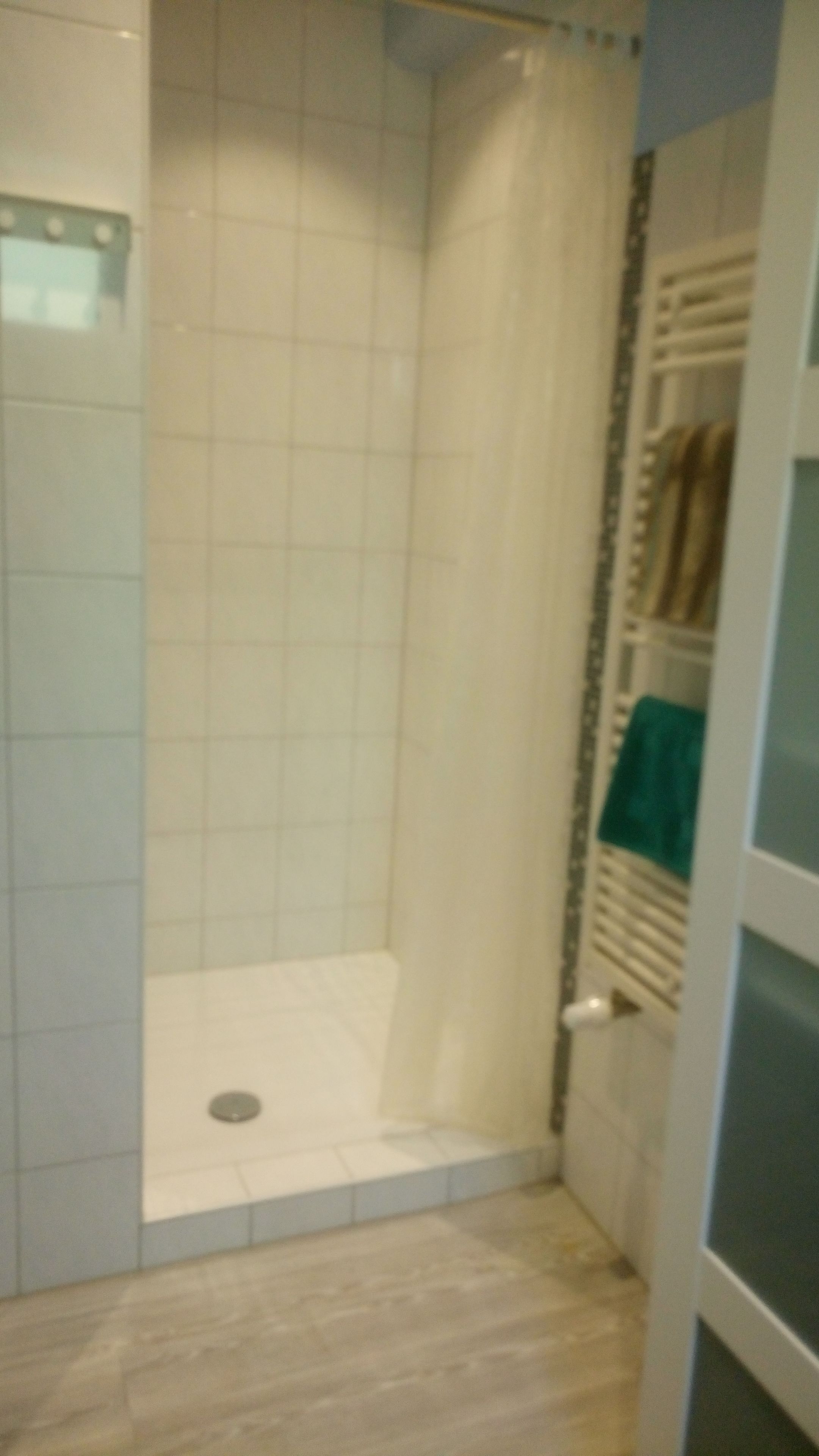 A small, enclosed shower area with tiled walls and a wooden floor.