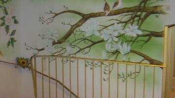 A room with a mural of a tree with white flowers and a bird, a metal gate, and two yellow vases.