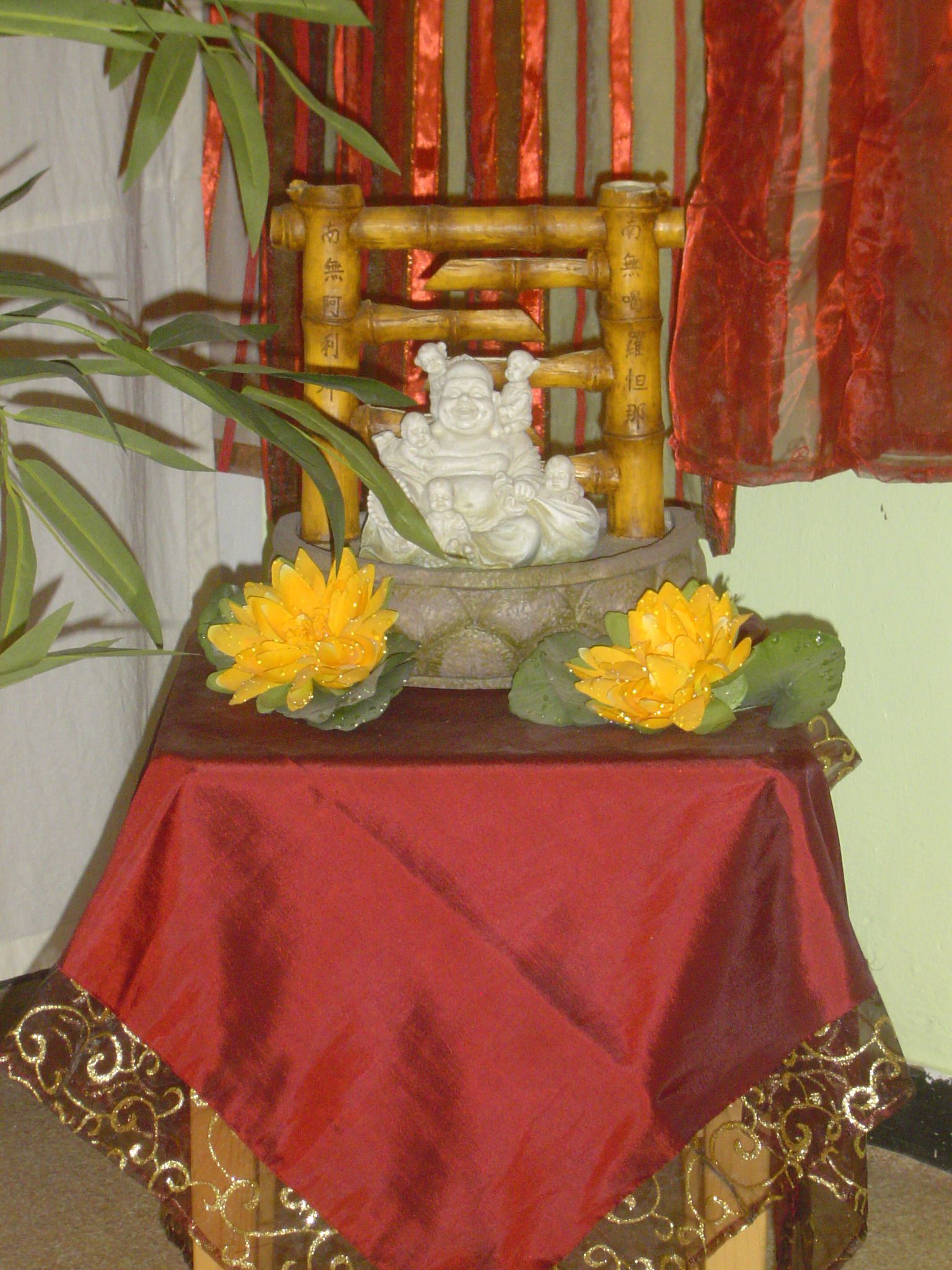 Une table recouverte d’une nappe rouge, une statue de Bouddha et deux fleurs de lotus.