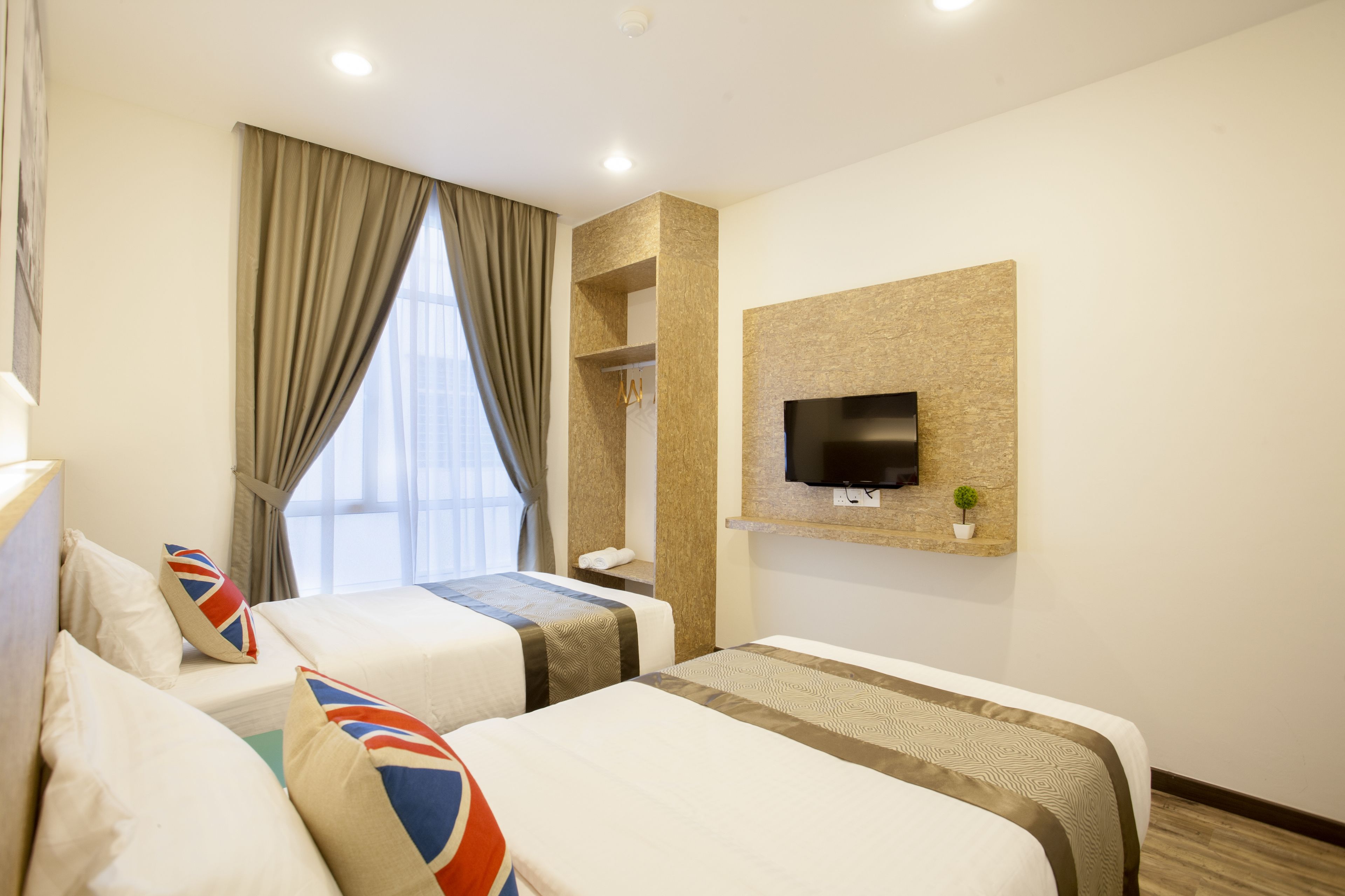 A hotel room with two beds, a flat-screen TV mounted on the wall, a small potted plant, and a window with curtains.