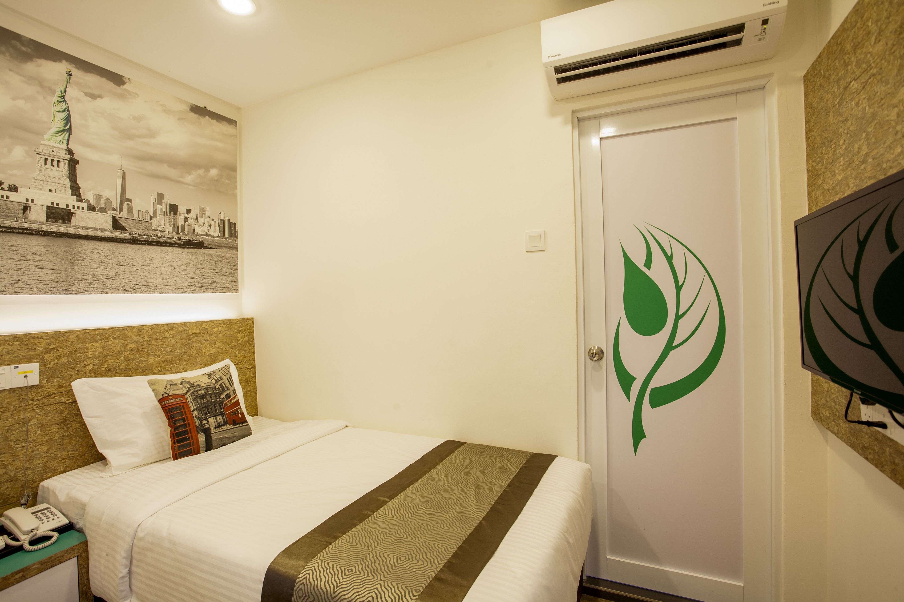 A hotel room with a bed, a telephone, a wall-mounted TV, and a door with a green leaf design.