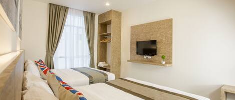 Een hotelkamer met twee bedden, een aan de muur bevestigde televisie, een plank met kleding en een raam met gordijnen.