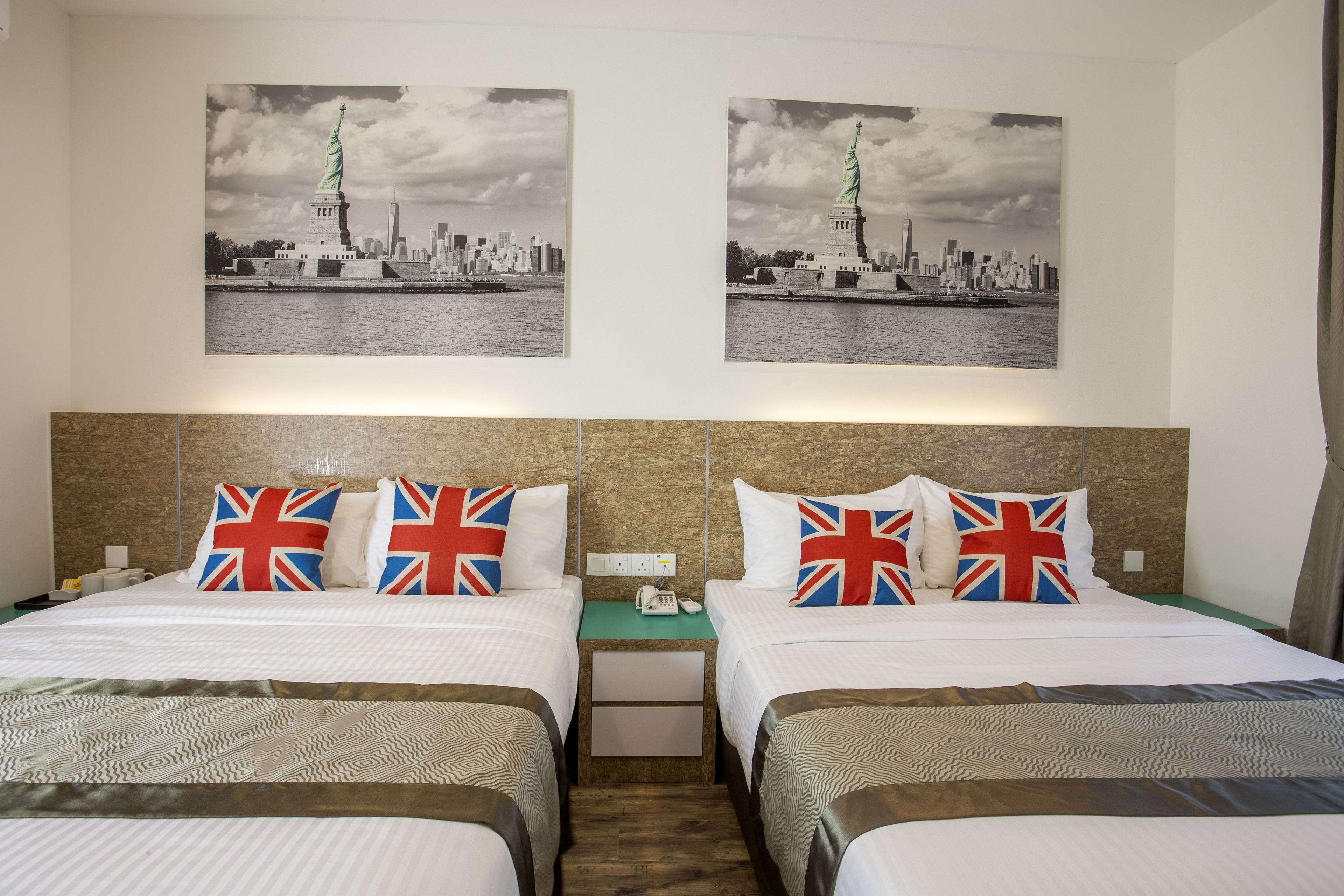 A hotel room with two beds, each with a British flag pillow, a headboard, and two black-and-white cityscape pictures on the wall.