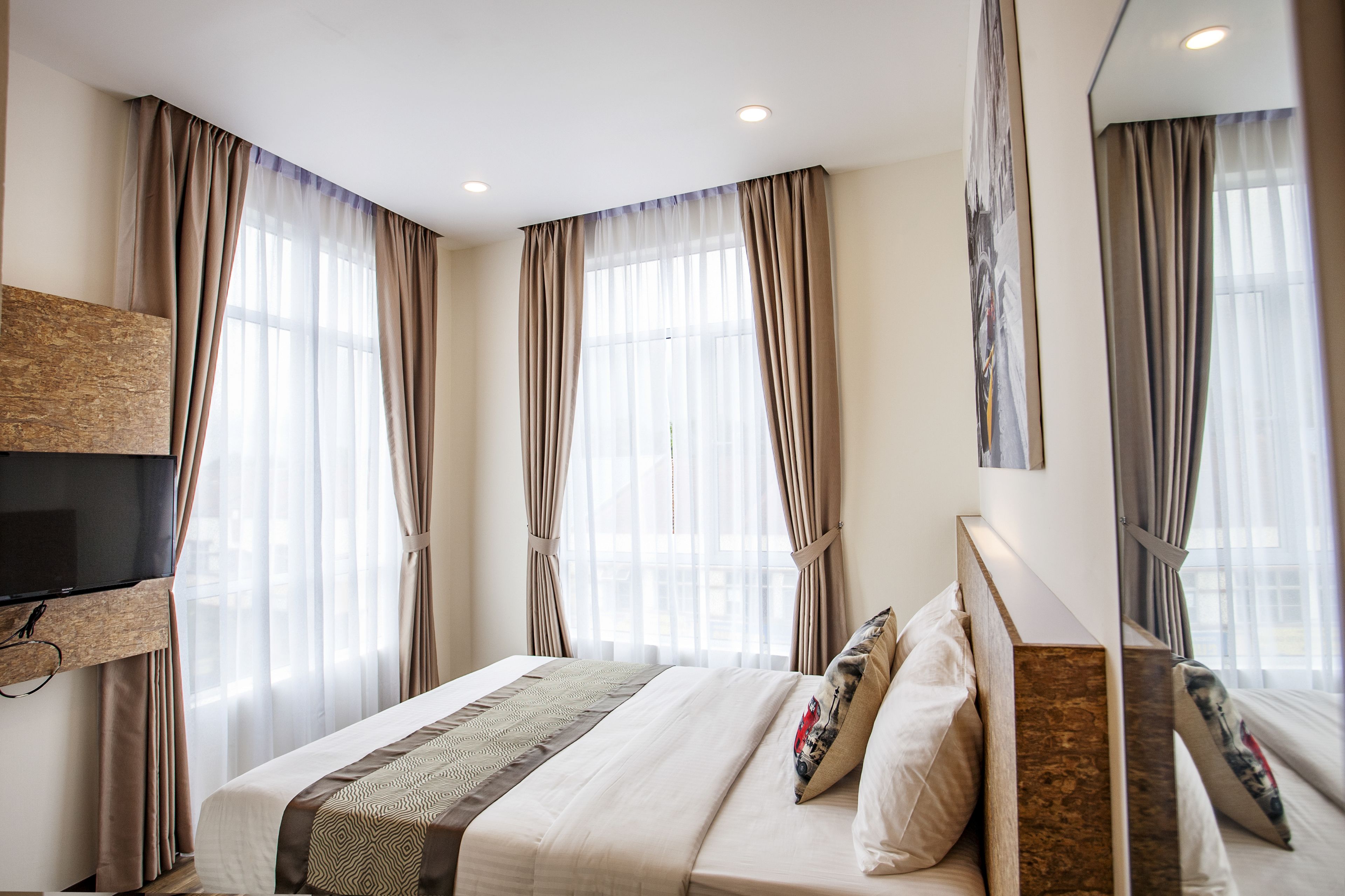 A hotel room with a large bed, a flat-screen TV mounted on the wall, and a large mirror.