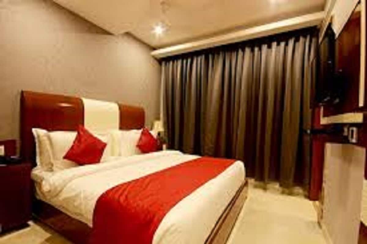 A hotel room with a large bed, red and white bedding, a wooden headboard, a nightstand, and a window with curtains.