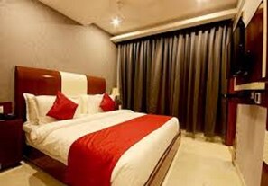 A hotel room with a large bed, red and white bedding, a wooden headboard, a nightstand, and a window with curtains.