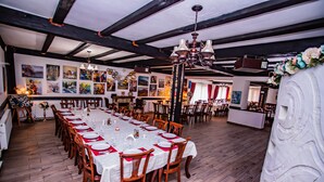 A long dining table set with white tablecloths and red napkins, surrounded by wooden chairs. - Casa Octavian (Sucevita)