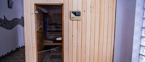 A wooden sauna with a control panel, a glass door, and a pebble floor.
