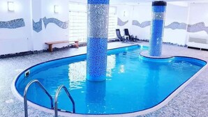 An indoor swimming pool with clear blue water, surrounded by tiled walls and a pebble floor. - Casa Octavian (Sucevita)