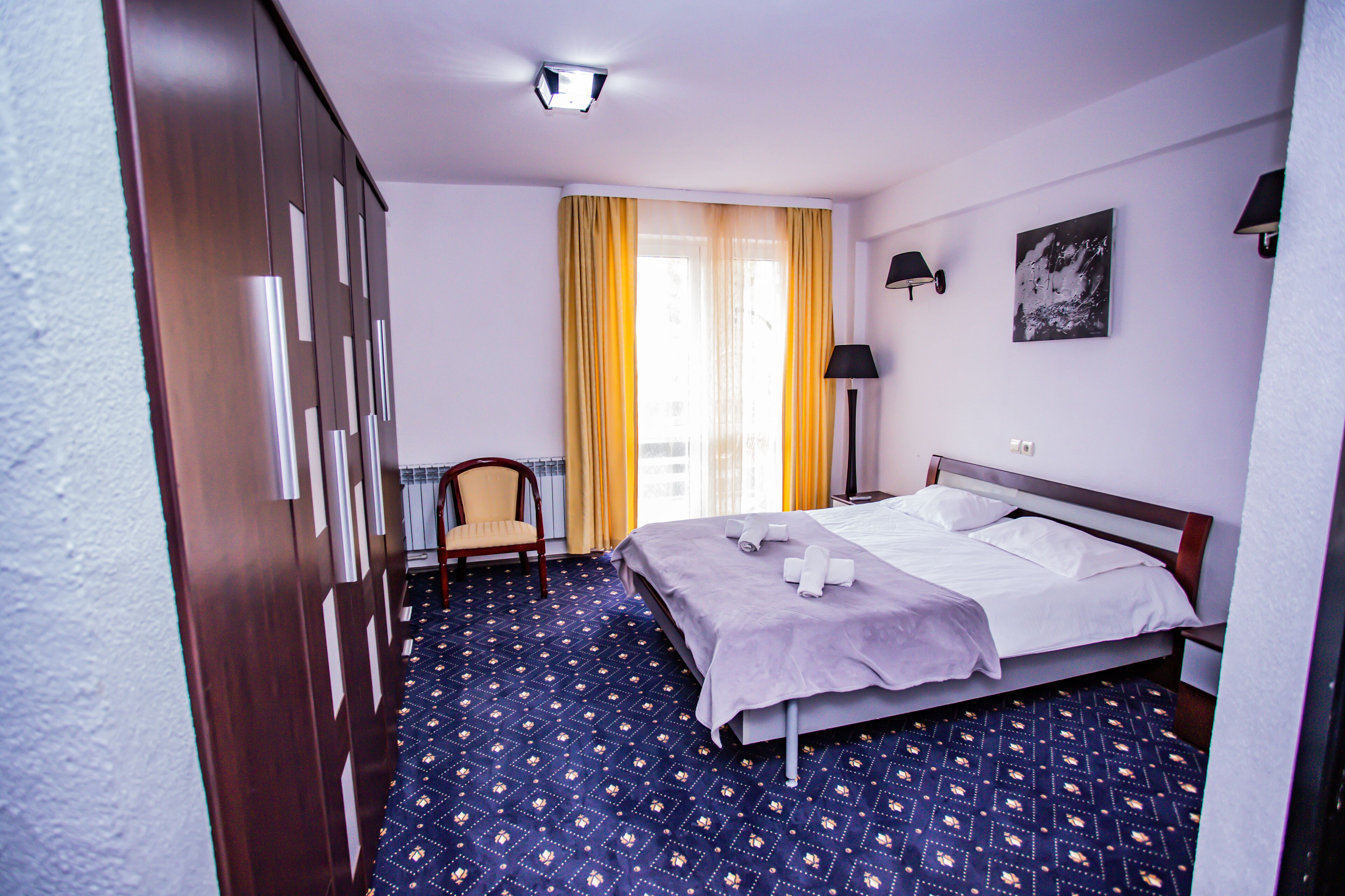 A hotel room with a bed, a chair, a desk, and a window with curtains.