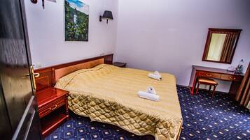 A hotel room with a bed, a desk, a chair, a dresser, and a painting on the wall.
