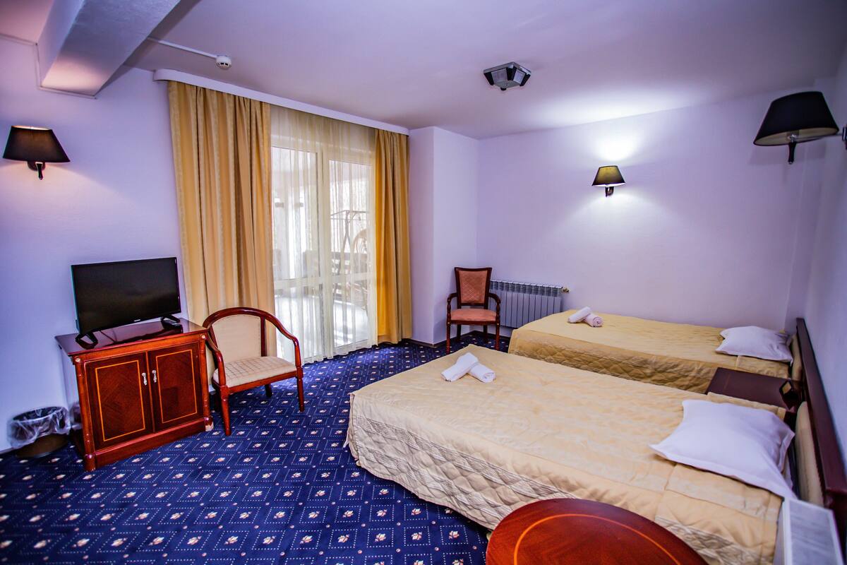 A hotel room with two beds, a television, a chair, and a desk.
