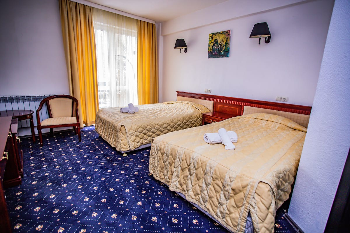 A hotel room with two beds, a chair, a desk, and a window with curtains.