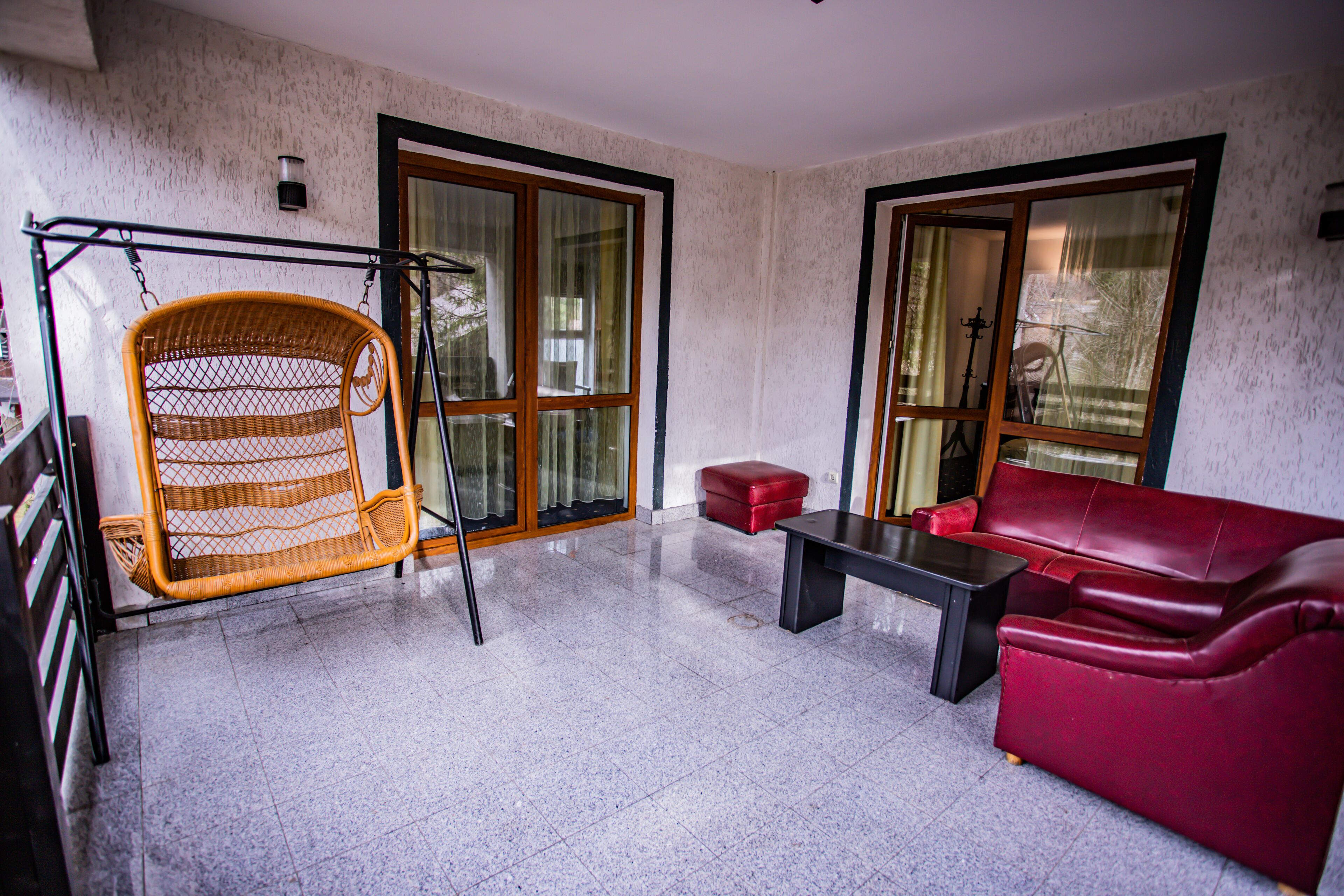 A room with a wicker chair, a red sofa, and a small table.