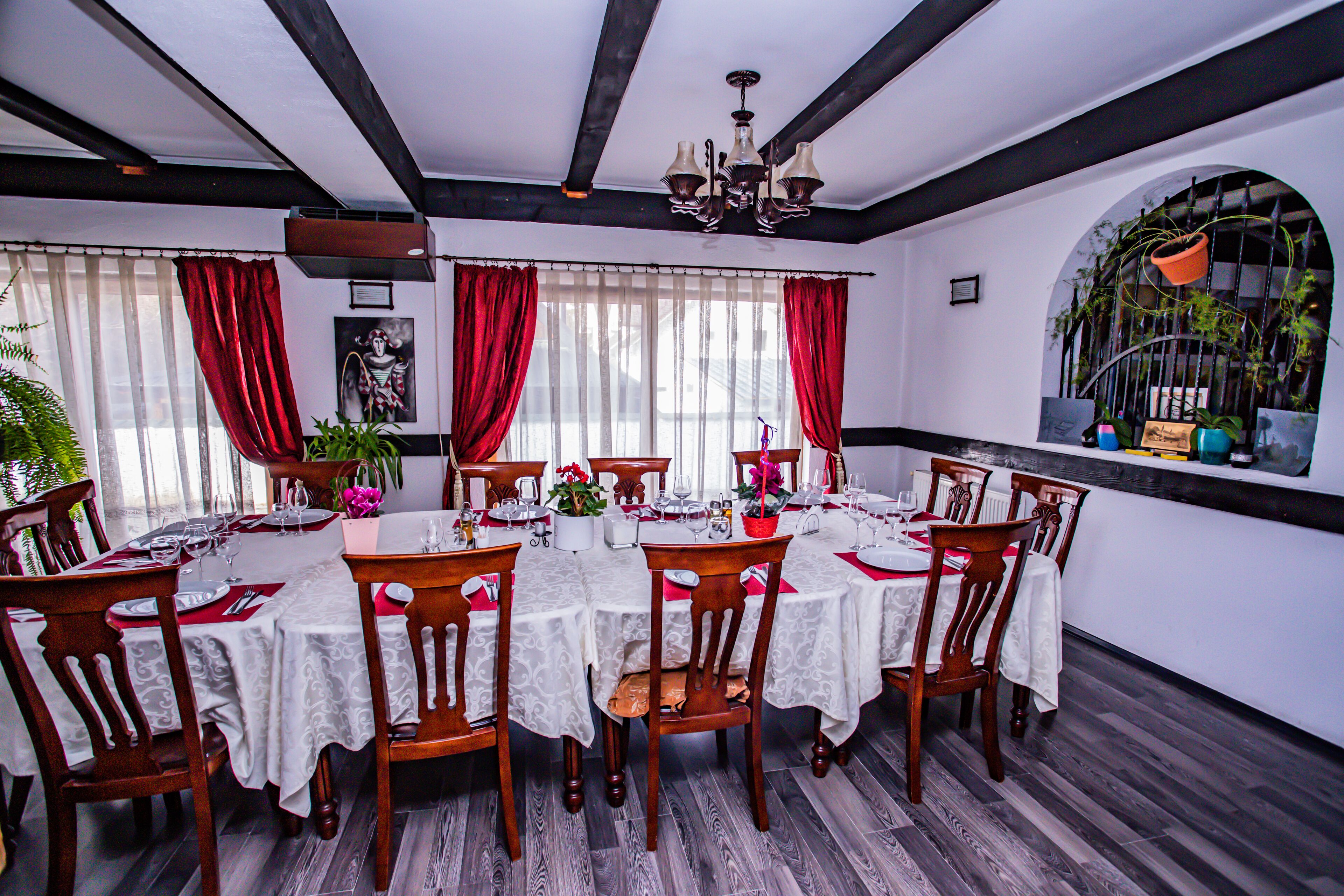 A dining room with a large table set for six, surrounded by wooden chairs, white tablecloths, and red curtains.