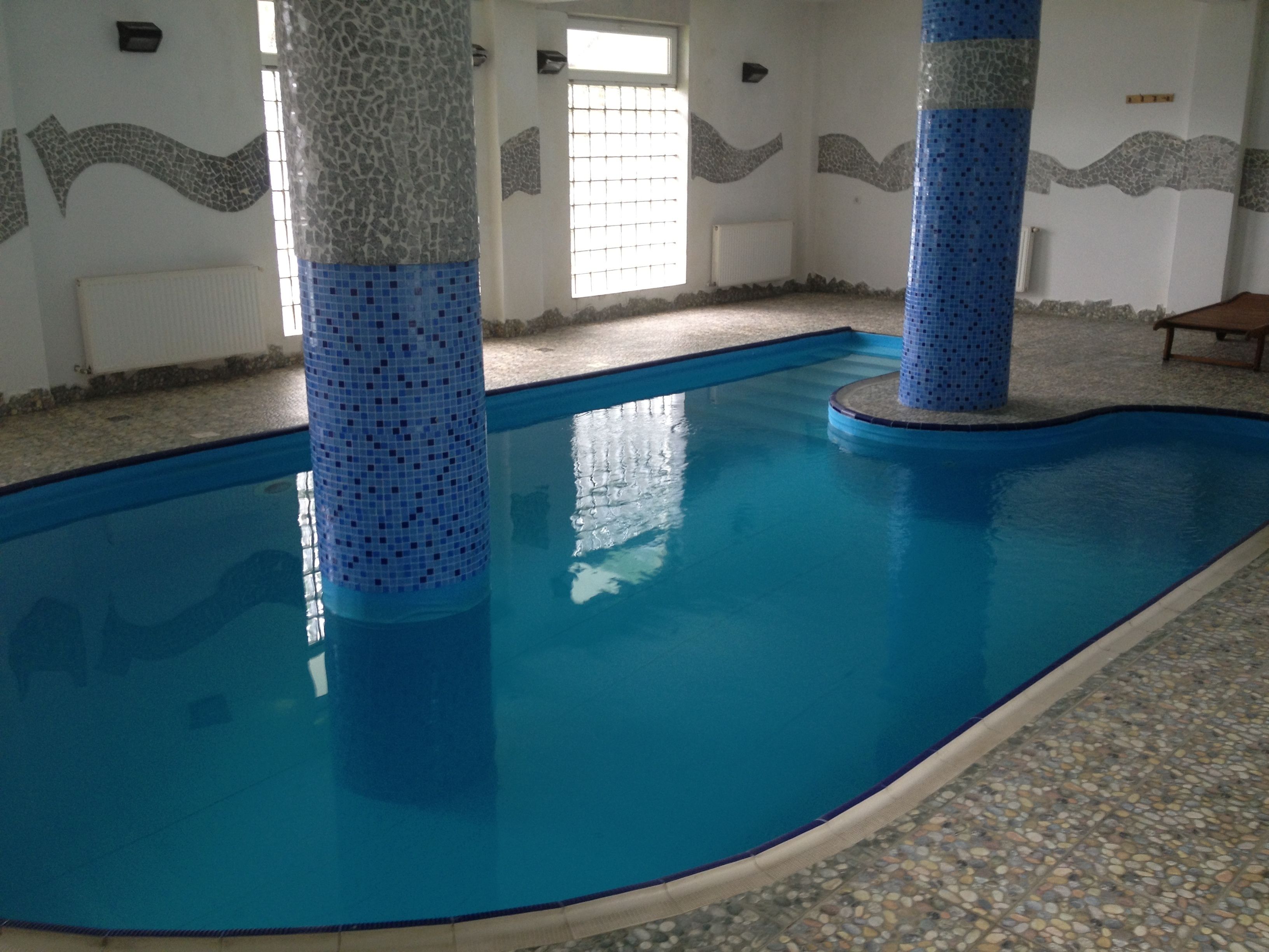 En inomhuspool med blå mosaikplattor, stenkolonner och ett golv av småsten.
