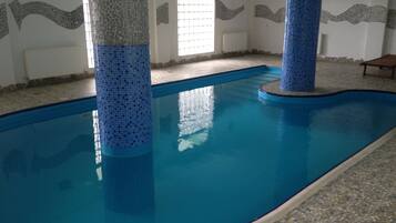 En inomhuspool med blå mosaikplattor, stenkolonner och ett golv av småsten.