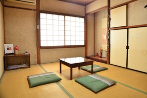A tatami mat room with a wooden table, green cushions, a window, and traditional sliding doors. - Biwako House (Otsu)