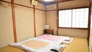 Una habitación japonesa tradicional con suelo de tatami, futón, mesita de noche de madera y pantalla shoji.