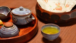 Un juego de té tradicional con tetera, tazas y un cuenco pequeño sobre una bandeja de madera.