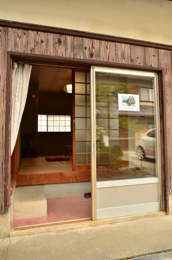 A traditional Japanese room with tatami flooring, a sliding door, and a view of the street. - Biwako House (Otsu)