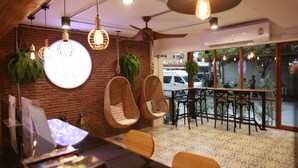 A modern interior with hanging lights, wicker chairs, a round table, and a view of the street outside. - Adagio Bangkok (Bangkok)