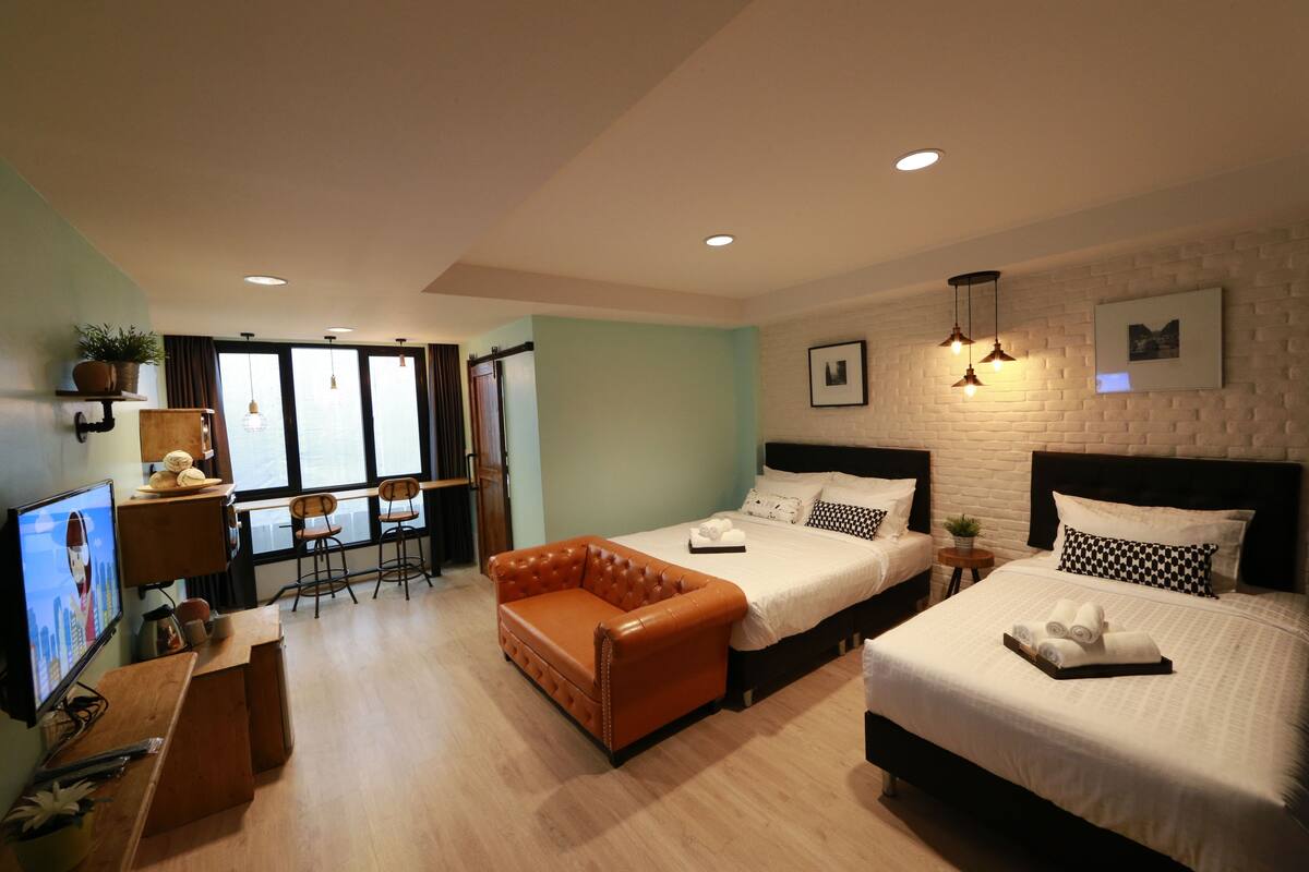 Une chambre d’hôtel avec deux lits, un canapé, un bureau avec un ordinateur et une télévision.