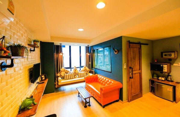 A compact living space with a sofa, a small table, a bench, a TV, a refrigerator, and a microwave. - Adagio Bangkok (Bangkok)