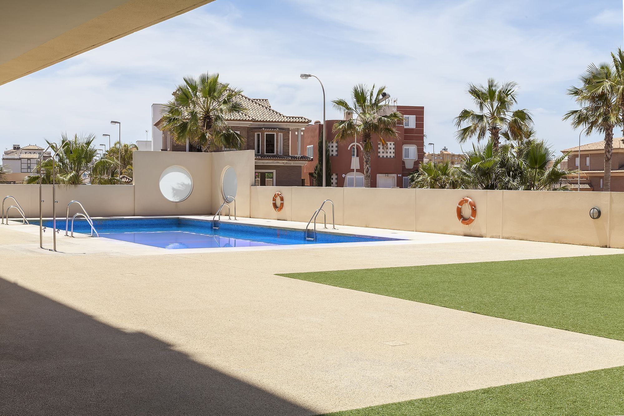 Una piscina con un flotador salvavidas, rodeada de palmeras y un edificio con tejado de baldosas.