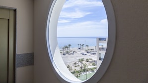 A view through a window of a building with a parking lot, palm trees, and a clear sky. - Apartamentos Mar y Sal (Roquetas de Mar)