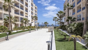 A modern hotel with a central courtyard, palm trees, and a view of the ocean. - Apartamentos Mar y Sal (Roquetas de Mar)
