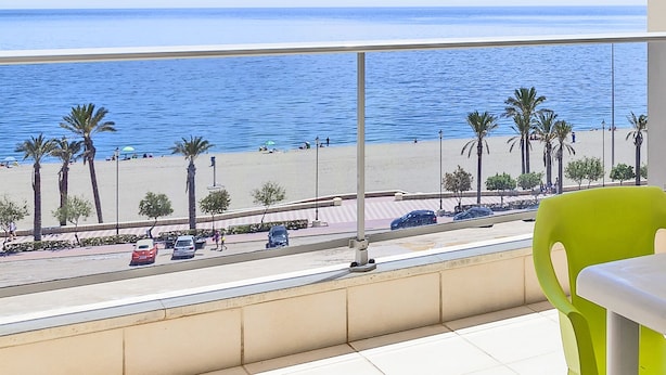 A balcony with a view of the beach, palm trees, and parked cars. - Apartamentos Mar y Sal (Roquetas de Mar)