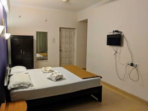 Habitació d'hotel amb un llit, un armari, una televisió penjada a la paret i una porta que dona a una altra habitació.