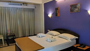Una habitación de hotel con una cama grande, una mesita de noche con lámpara y un aire acondicionado instalado en la pared.