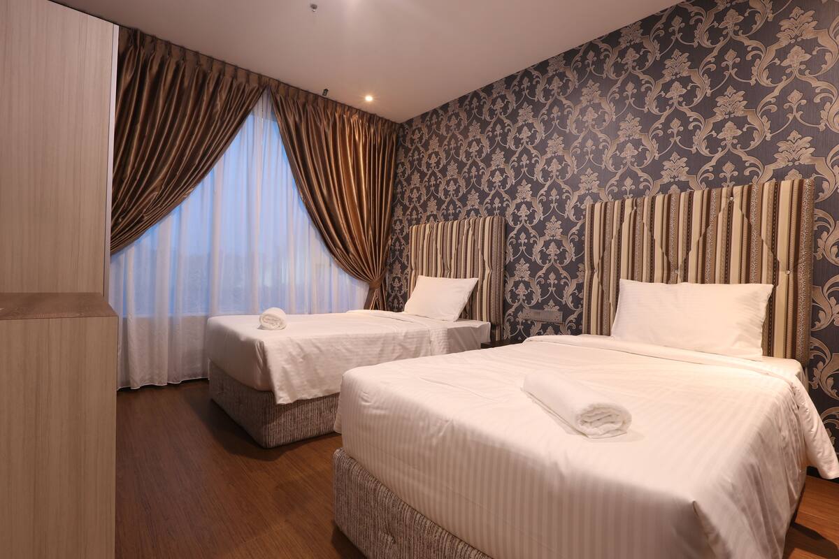 Une chambre d’hôtel avec deux lits, une grande fenêtre avec des rideaux, un papier peint à motifs et un plancher en bois.