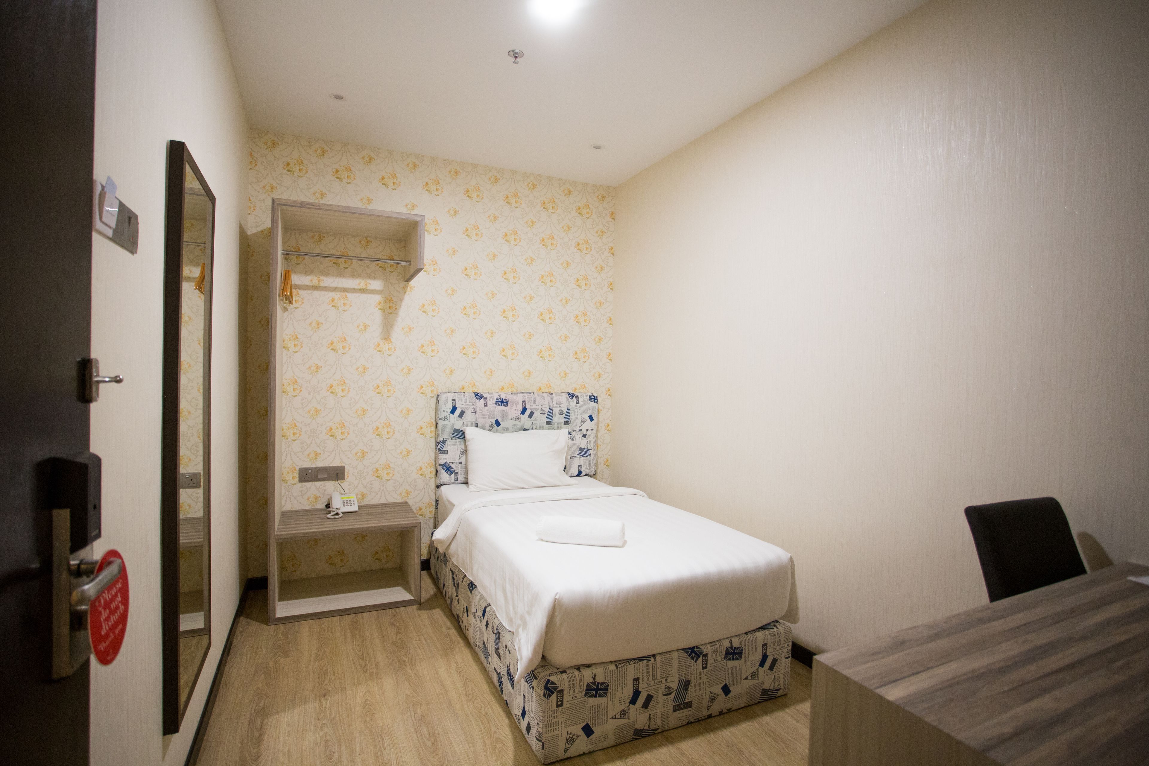 A small, neatly arranged bedroom with a single bed, a bedside table, and a mirror.