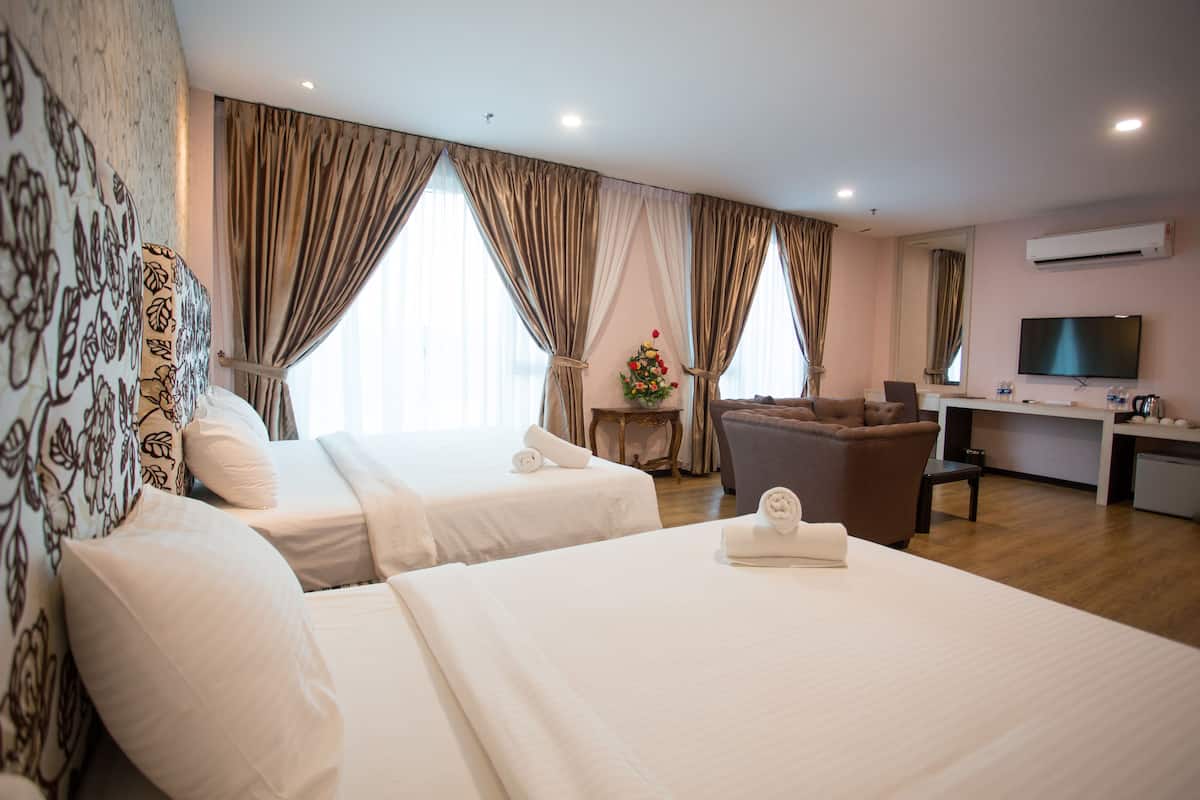 Une chambre d’hôtel avec deux lits, un canapé, une télévision et une petite table agrémentée d’un arrangement floral.