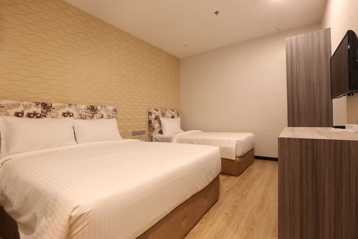Une chambre d’hôtel avec un grand lit, deux petits lits, un plancher en bois, une télévision et un mur décoré d’un motif.