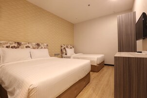 Habitación de hotel con una cama grande, dos camas más pequeñas, piso de madera, televisión y un papel tapiz estampado.