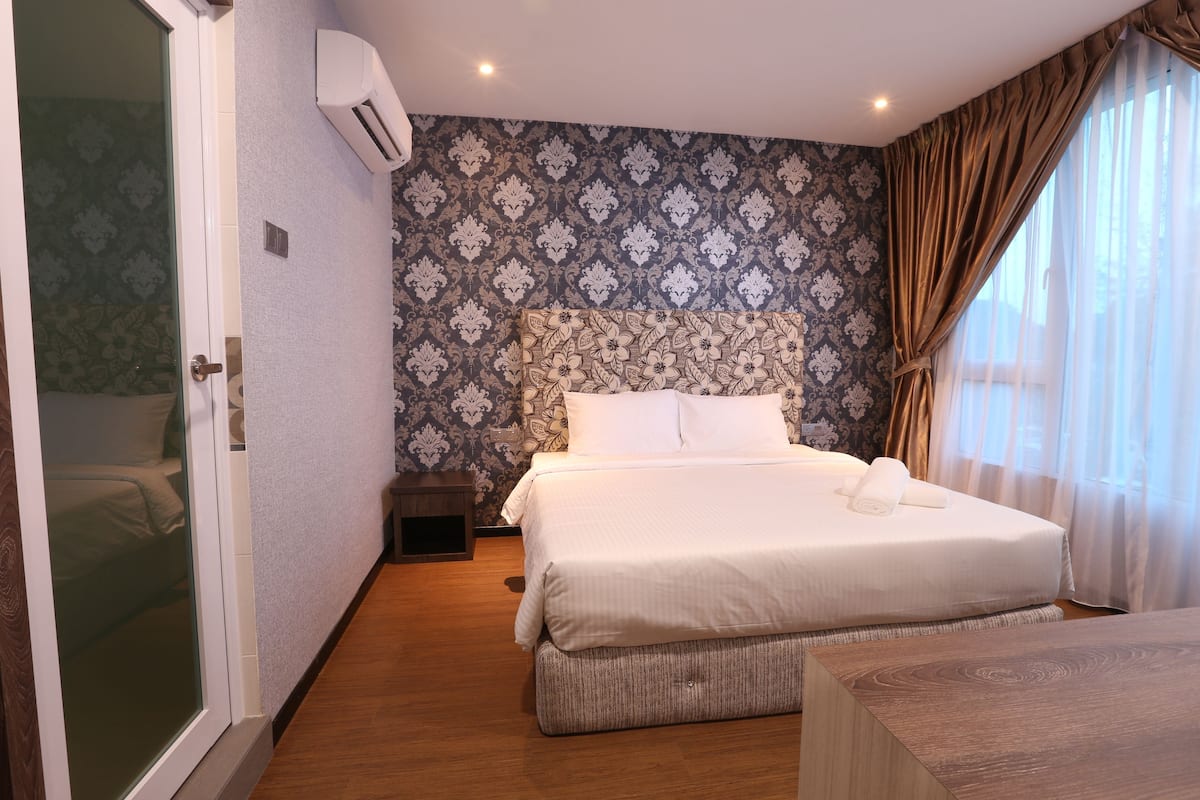 Une chambre d’hôtel avec un grand lit, une table de chevet, une petite commode et une fenêtre avec des rideaux.