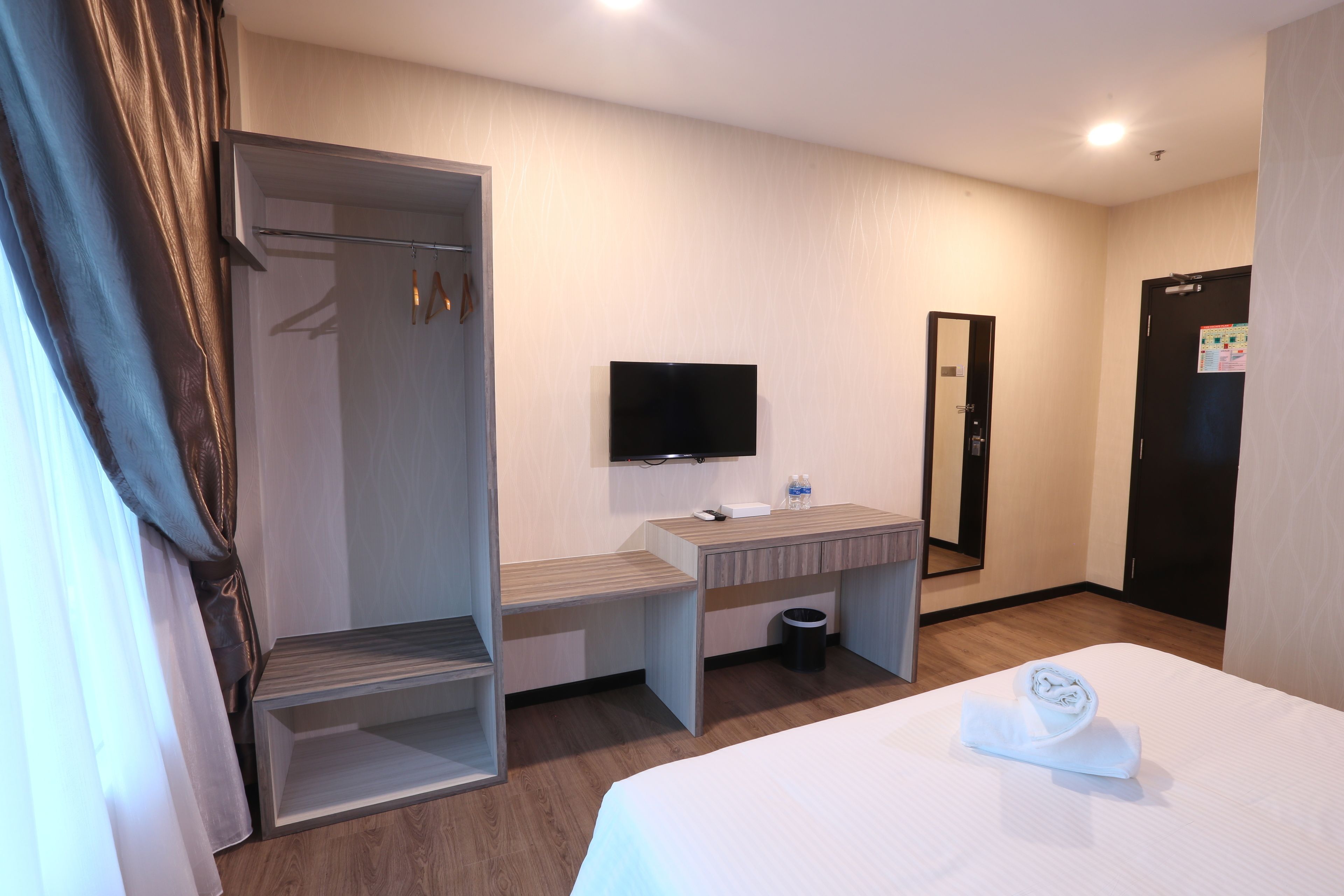 A hotel room with a bed, a desk with a computer, a TV, a mirror, and a wardrobe.