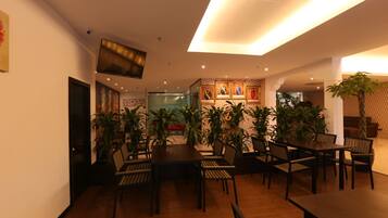 A dining area with wooden tables and chairs, surrounded by potted plants.
